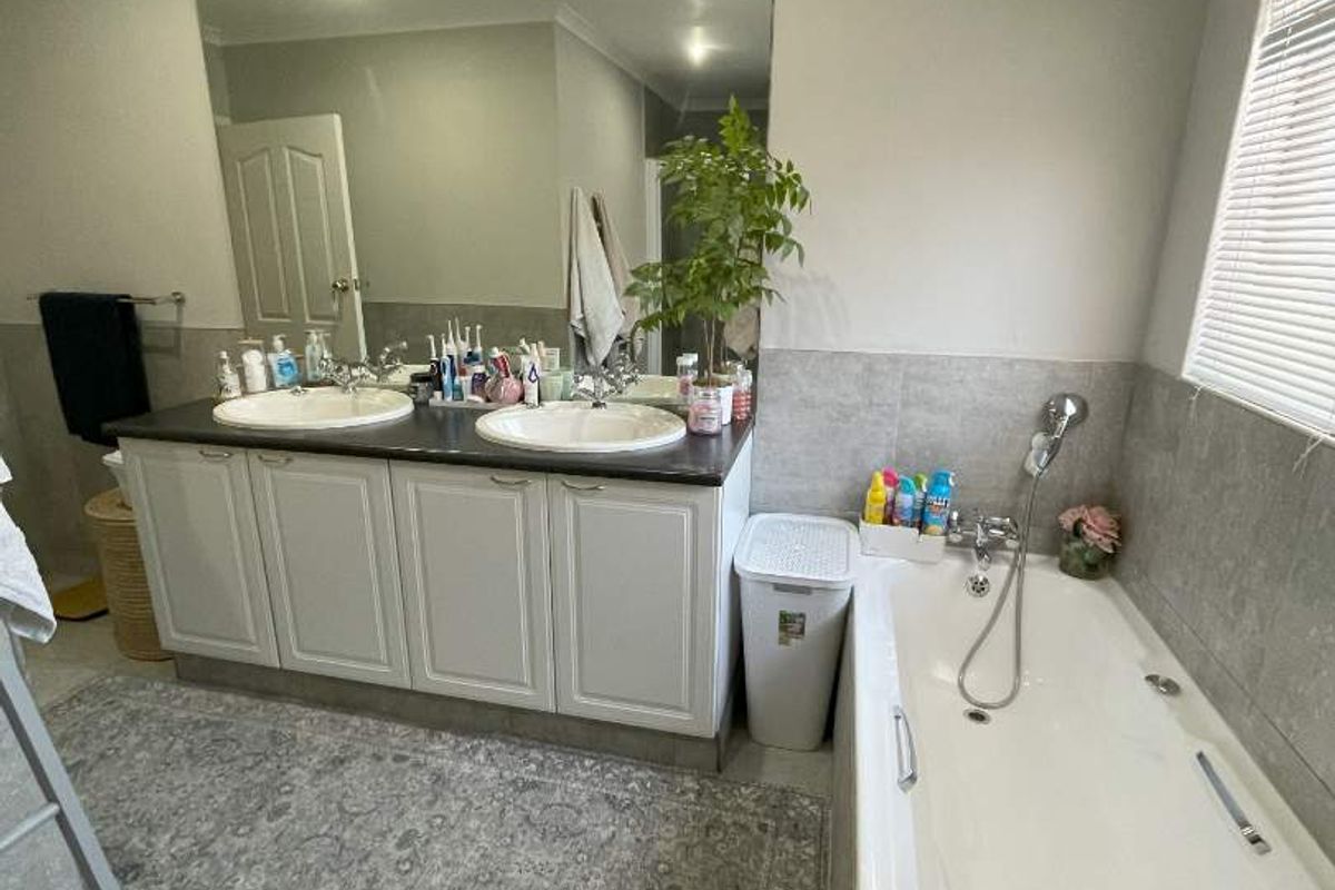A functional bathroom featuring a double vanity with a large mirror, a built-in bathtub, and neutral tiled finishes.
