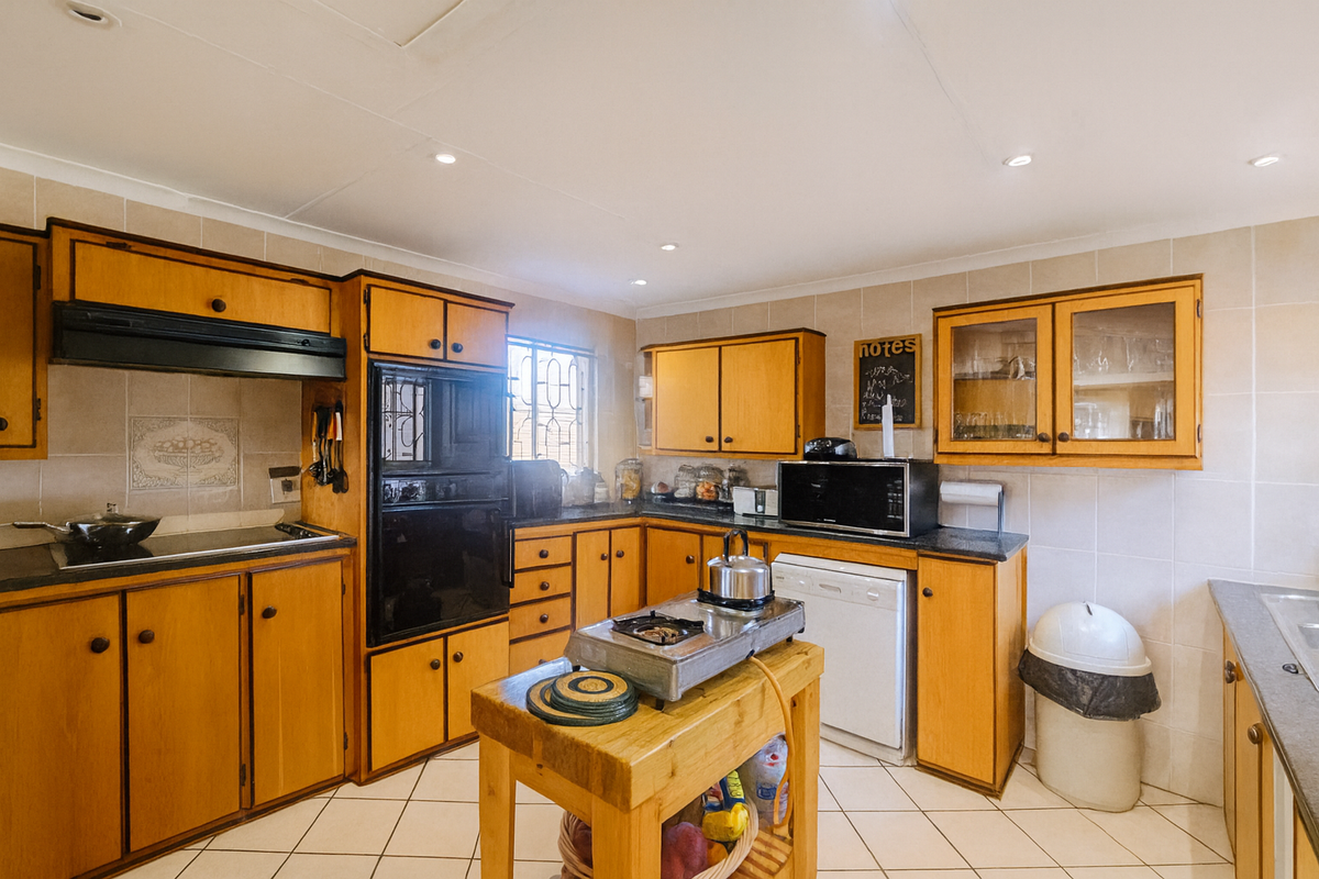 A functional kitchen featuring wooden cabinetry, built-in oven, extractor fan, and tiled flooring, offering a classic layout with ample storage space.