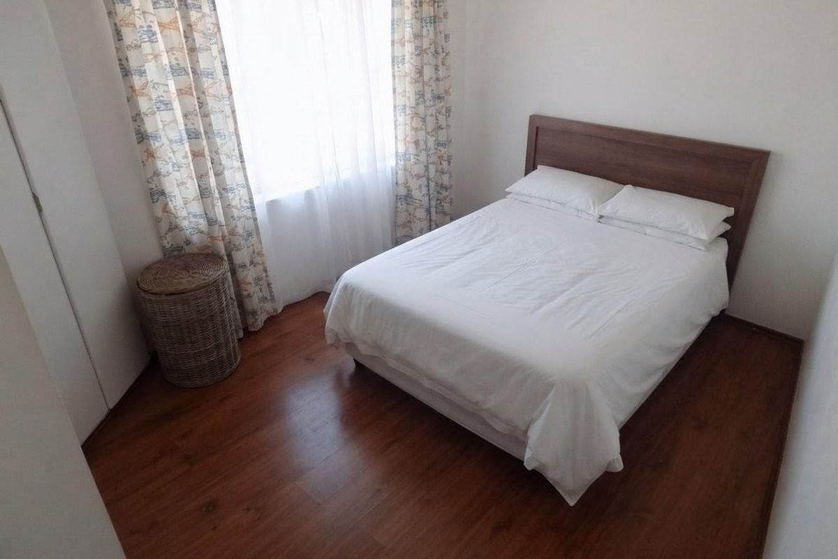 A compact bedroom featuring laminate flooring and a built-in wardrobe, providing a functional and neutral living space.