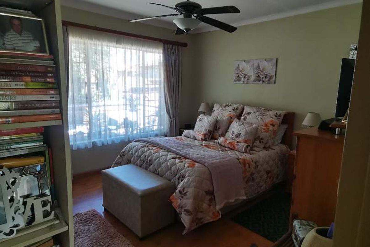 A cozy bedroom featuring wood-look flooring, a ceiling fan, and a large window with natural light.