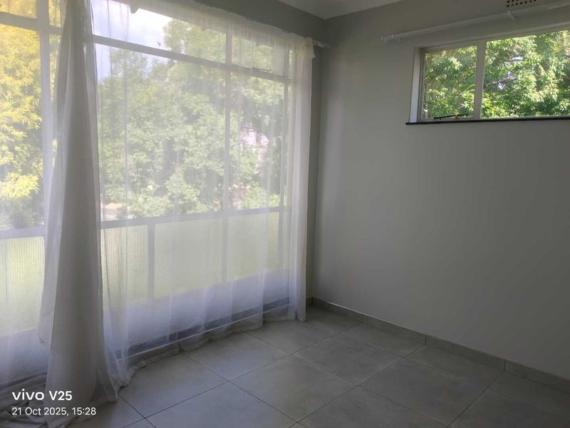 A bright, empty bedroom featuring large windows with natural light, neutral wall paint, and clean tiled flooring, ready for personalization.