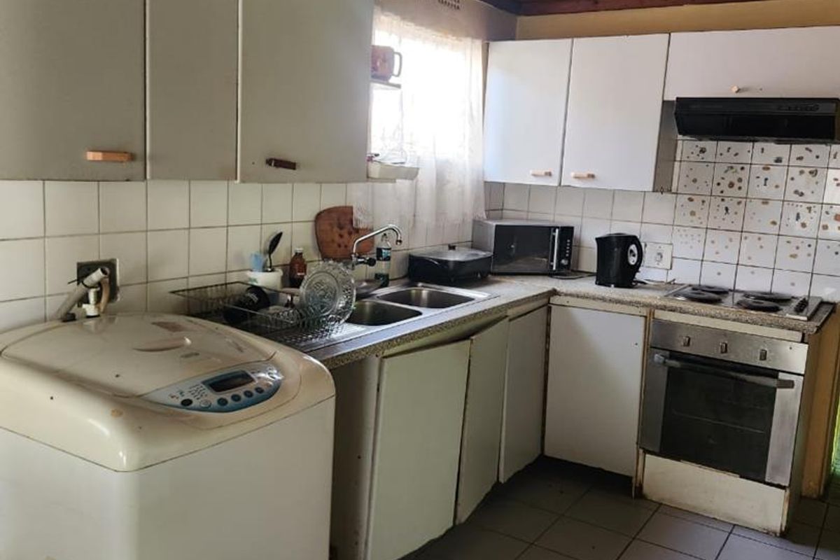 A dated kitchen featuring white cabinetry, a tiled backsplash, built-in oven and hob, and integrated laundry plumbing.