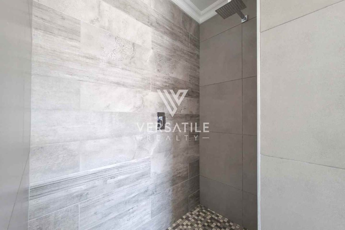 Modern walk-in shower featuring contemporary grey wall tiles, a rainfall showerhead, and a mosaic-tiled floor.