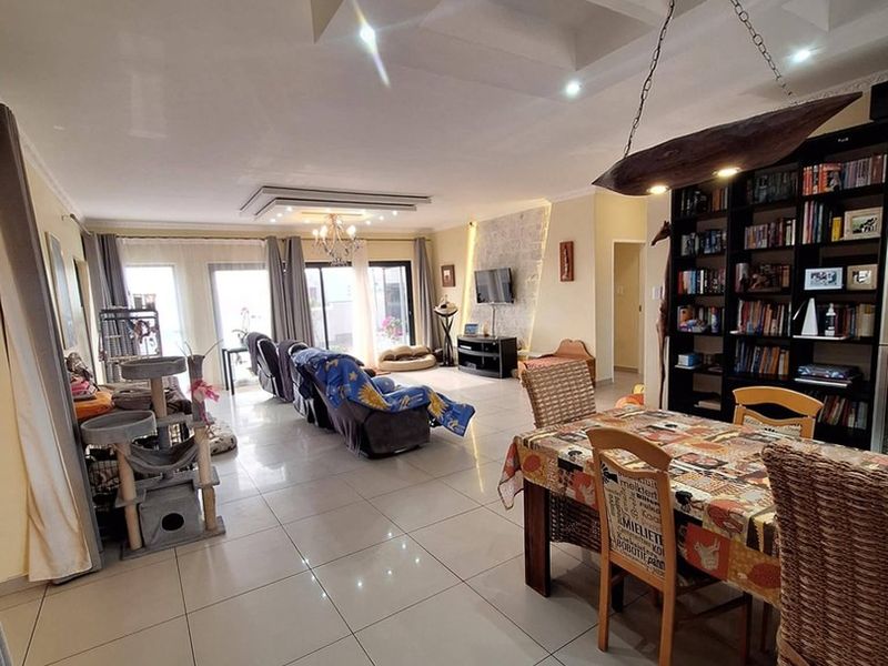 Spacious open-plan living and dining area featuring large format floor tiles, recessed ceiling details, and integrated shelving, offering a bright and versatile layout.