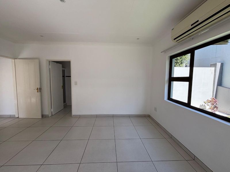 A bright, empty bedroom featuring neutral tiled flooring, recessed lighting, and a wall-mounted air conditioning unit.