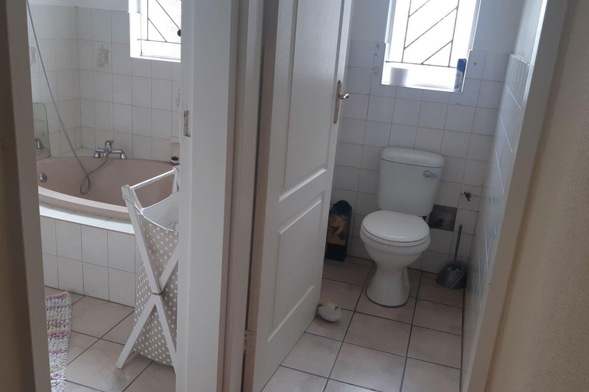 A dated bathroom featuring a built-in bathtub and separate toilet area with ceramic tiling throughout, requiring cosmetic updates to modernize the space.