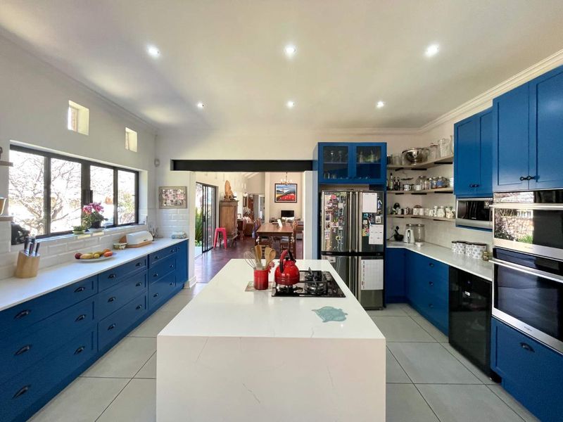Modern kitchen featuring a large central island, stone countertops, blue cabinetry, built-in appliances, and subway tile backsplash, opening into the dining area.