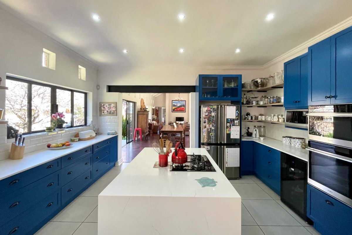 Modern kitchen featuring a large central island, stone countertops, blue cabinetry, built-in appliances, and subway tile backsplash, opening into the dining area.