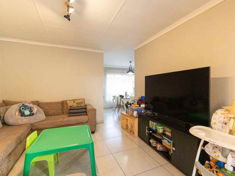 A living room area featuring tiled flooring, coved ceilings, and track lighting, with an open-plan layout leading towards the dining space.