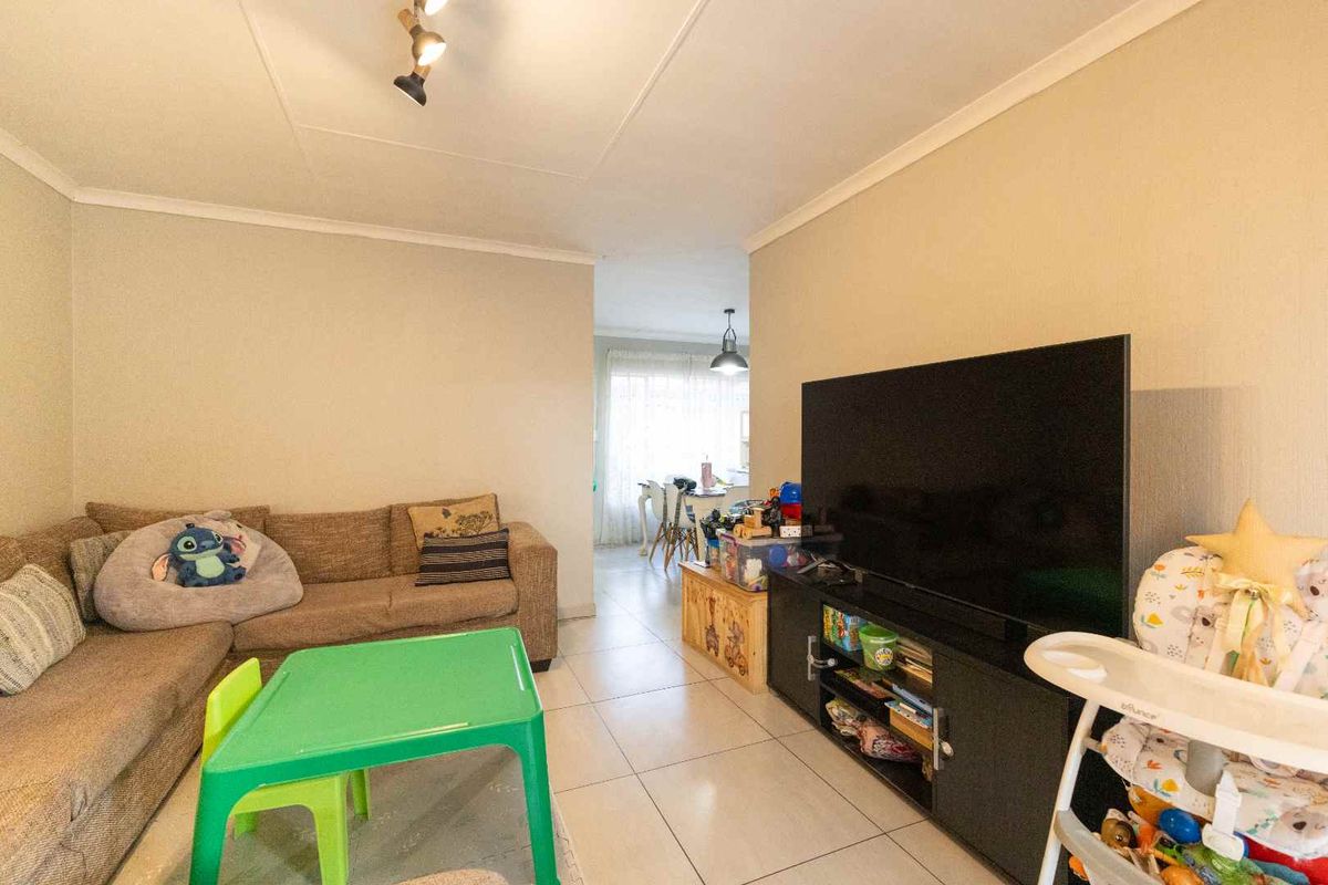 A living room area featuring tiled flooring, coved ceilings, and track lighting, with an open-plan layout leading towards the dining space.
