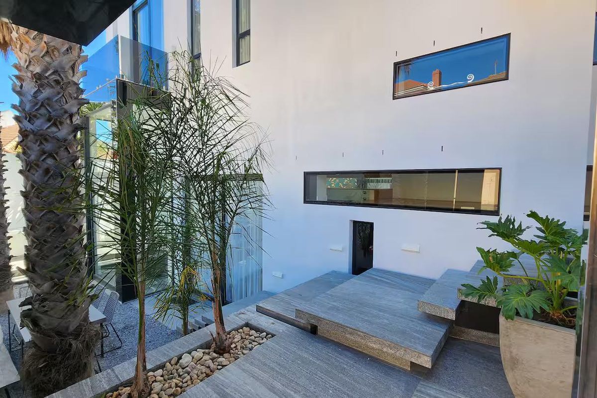 A modern rear exterior terrace featuring stone paving, integrated planter boxes, and architectural horizontal windows, creating a clean and contemporary outdoor living space.