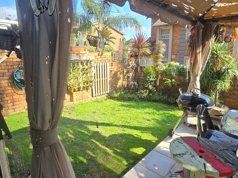 A private outdoor patio area featuring tiled flooring, a covered structure, and a small garden space enclosed by brick boundary walls.