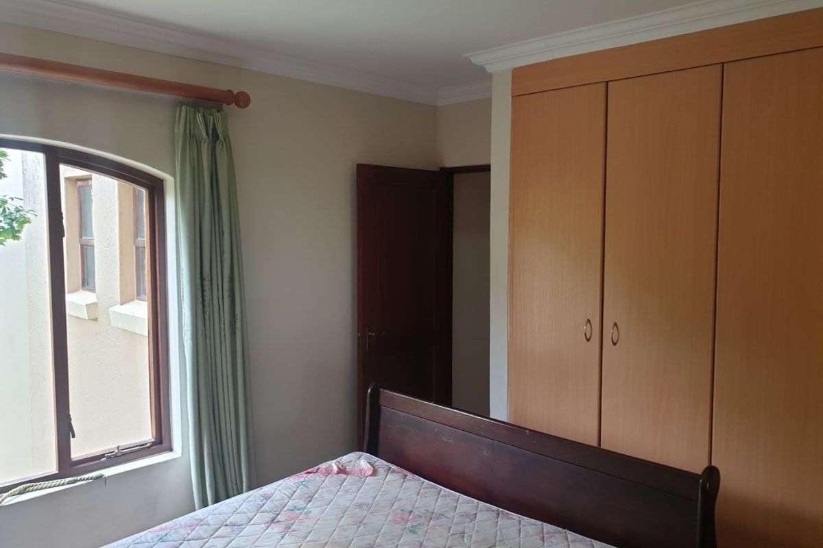 A bedroom featuring a built-in wooden wardrobe, an arched window, and decorative ceiling cornicing.