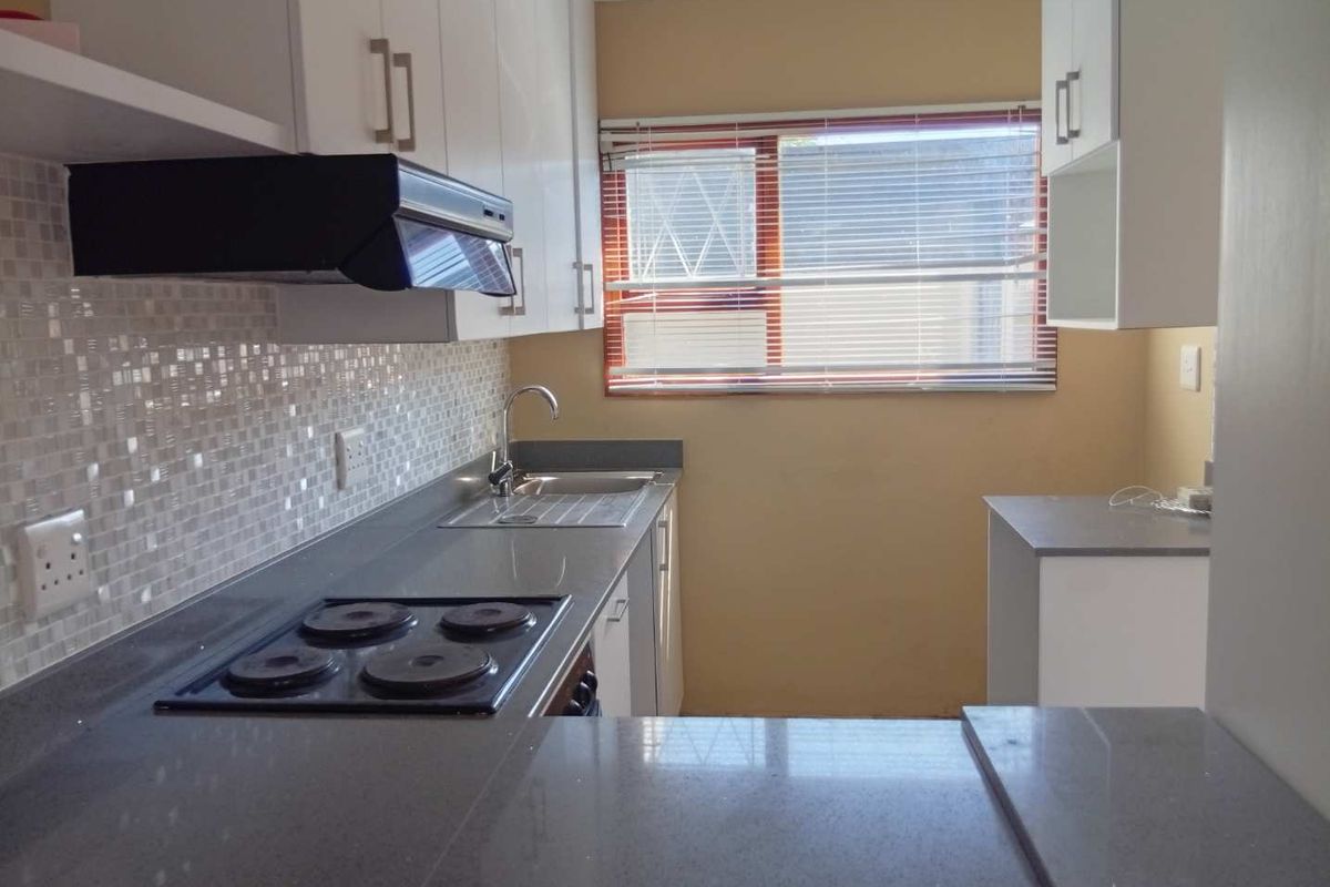 A clean, functional kitchen featuring white cabinetry, grey stone countertops, a mosaic tile backsplash, and a built-in electric hob with an extractor fan.