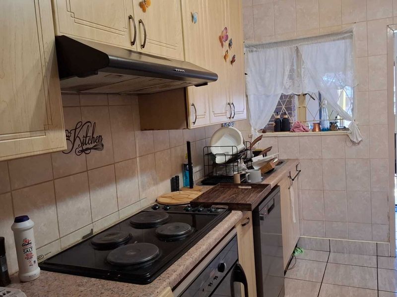 A functional kitchen featuring built-in cabinetry, an electric hob with extractor fan, and tiled finishes throughout, providing a practical workspace for daily cooking.