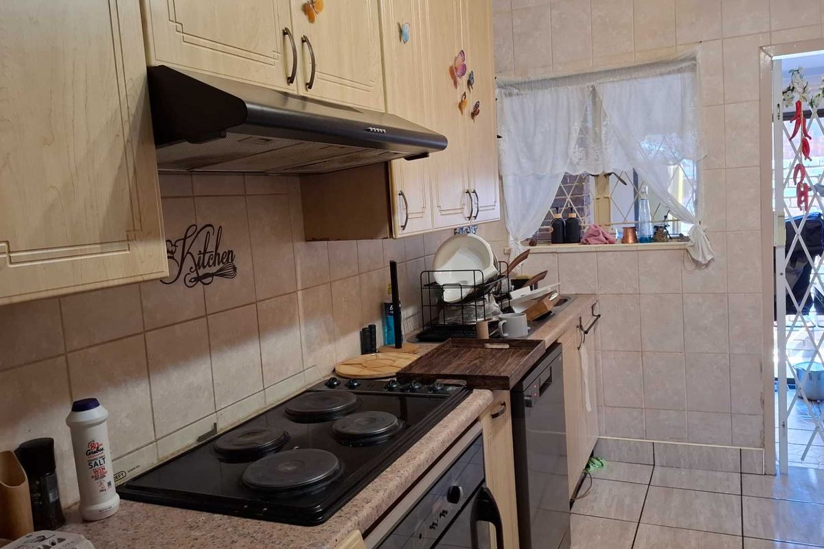 A functional kitchen featuring built-in cabinetry, an electric hob with extractor fan, and tiled finishes throughout, providing a practical workspace for daily cooking.