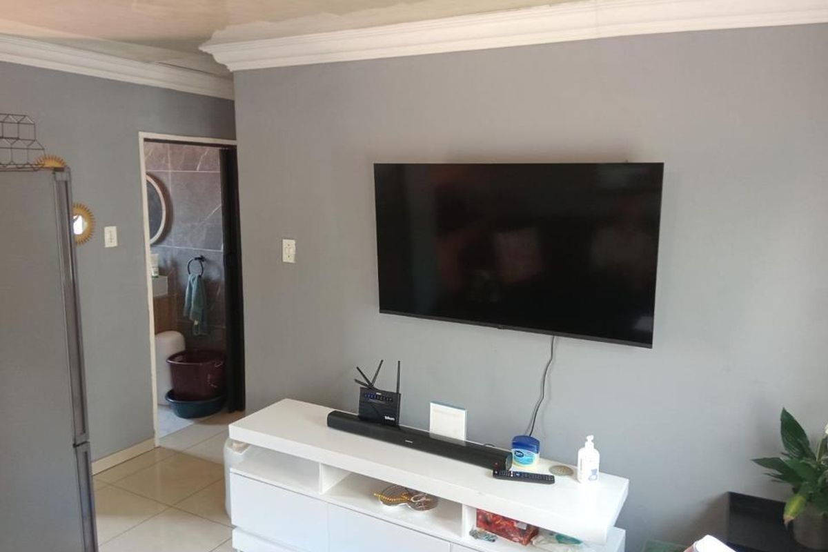 A living room area featuring a wall-mounted television, tiled flooring, and a view into an adjacent bathroom with tiled walls.