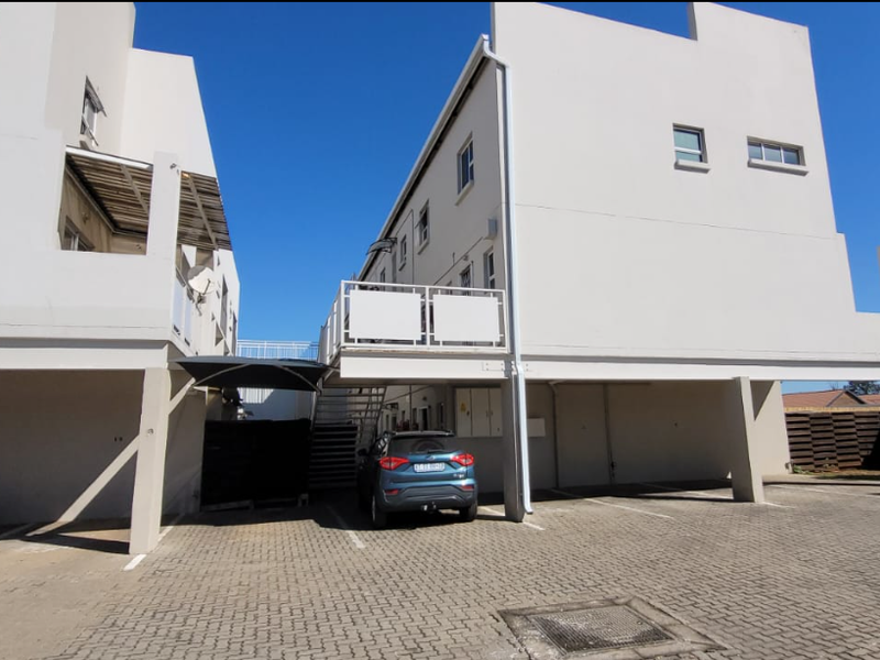 Exterior view of the apartment complex showing the paved parking area, ground-level covered parking bays, and external staircase leading to upper-level units.