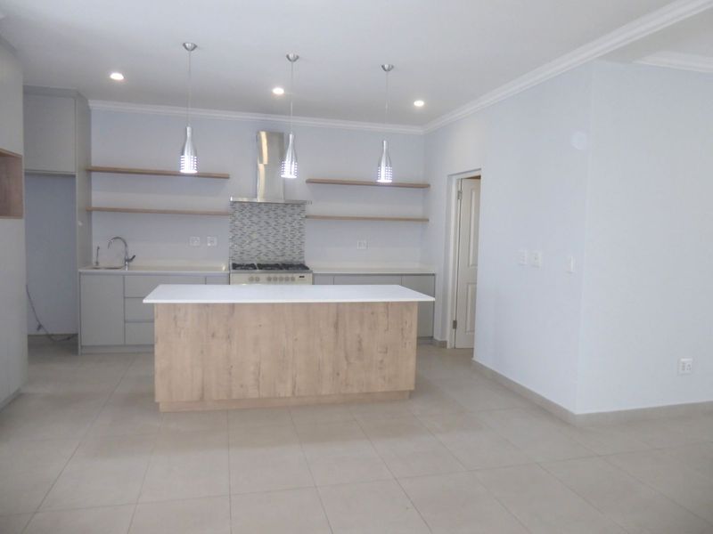 Modern kitchen featuring a central island, gas hob with extractor, floating shelving, and neutral tiled flooring in an open-plan layout.