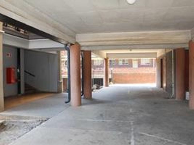 A covered parking area featuring concrete columns, flooring, and direct access to the building's stairwell.