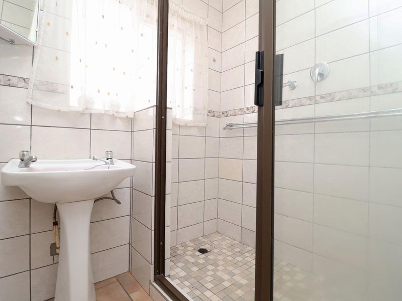 A functional bathroom featuring a pedestal basin and a separate shower enclosure with tiled walls and flooring.