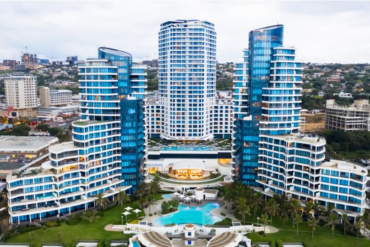 Aerial view of a modern high-rise apartment complex featuring glass facades, multiple balconies, landscaped grounds, and a central swimming pool area.