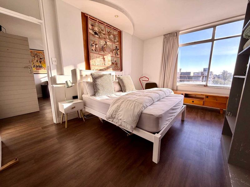 A bright and well-maintained bedroom featuring laminate flooring, recessed ceiling lighting, and a large window providing natural light.
