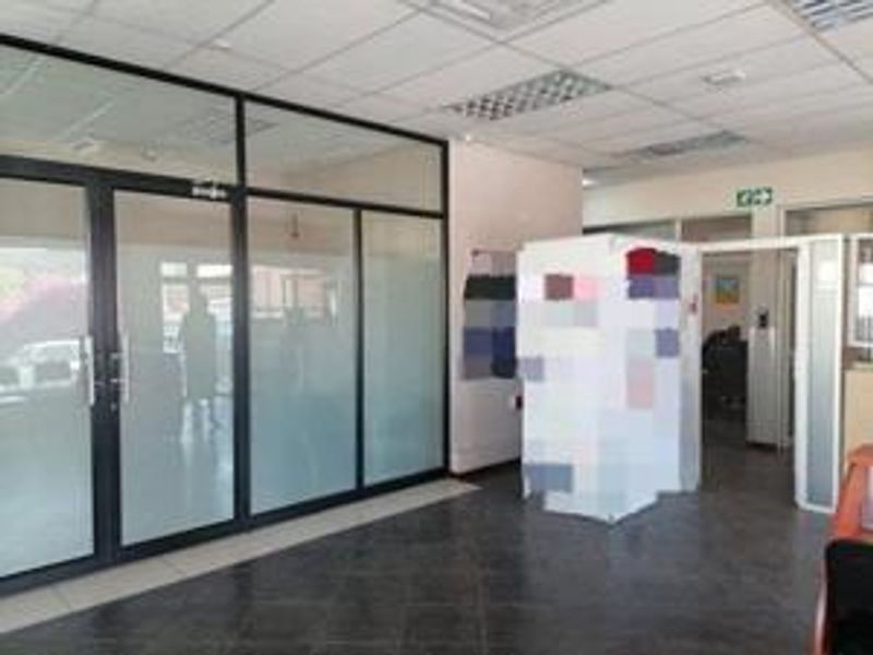 A functional office space featuring glass partition walls, suspended ceilings with recessed lighting, and durable tiled flooring.