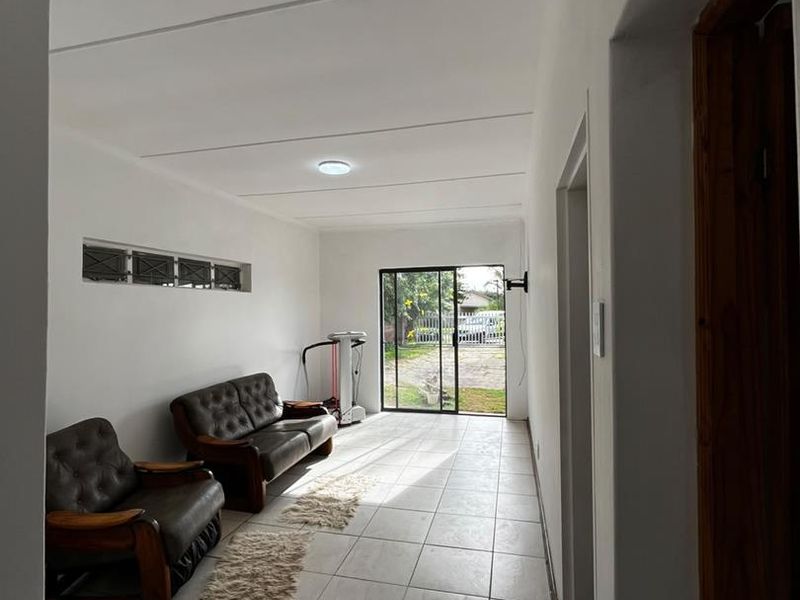 A bright living area featuring tiled flooring, a sliding glass door providing outdoor access, and natural light through high-set louvre windows.