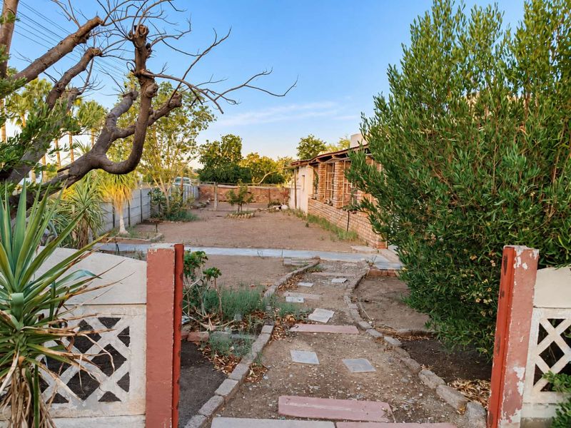 A rear garden area featuring a brick boundary wall, a concrete pathway, and a brick house facade, requiring landscaping and maintenance.