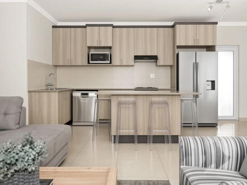 Modern open-plan kitchen featuring light wood cabinetry, stone countertops, a central island, and integrated appliances, seamlessly flowing into the living area.