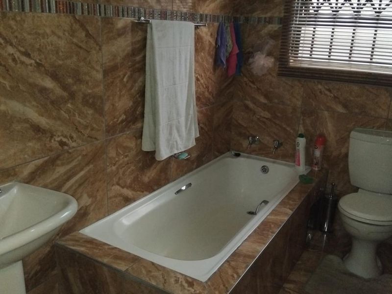 A functional bathroom featuring a built-in bathtub, pedestal basin, and toilet, finished with full-height brown marble-effect wall tiles.
