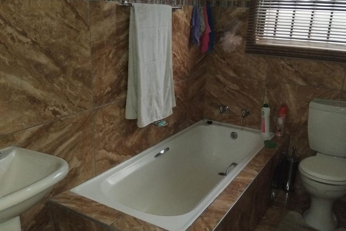 A functional bathroom featuring a built-in bathtub, pedestal basin, and toilet, finished with full-height brown marble-effect wall tiles.