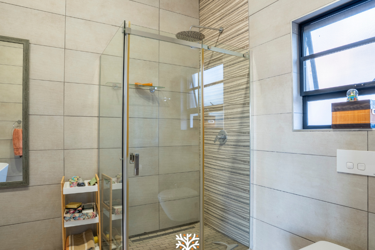 Modern bathroom featuring a glass-enclosed rain shower, wall-mounted toilet, and neutral large-format wall tiles with a decorative accent strip.