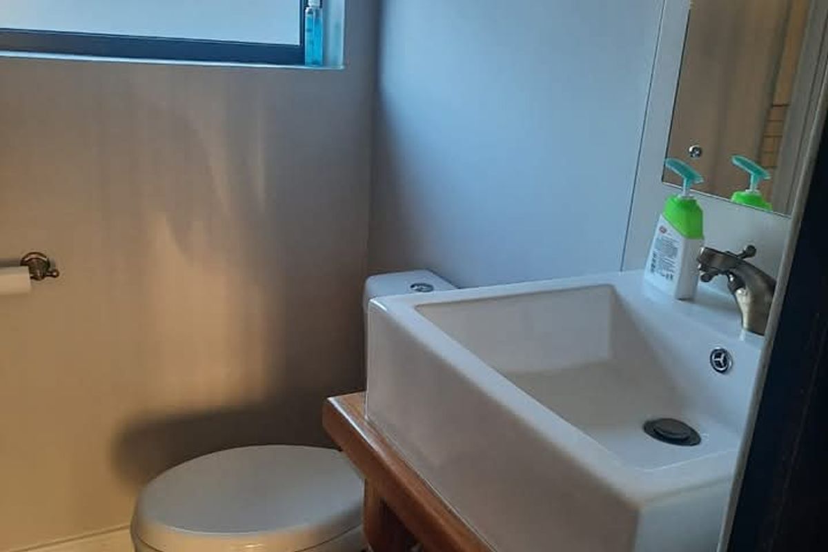 A compact bathroom featuring a modern square vessel sink on a wooden vanity, a standard toilet, and a window with a roller blind.