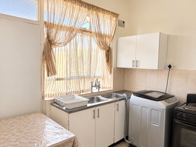 A functional laundry area featuring a double stainless steel sink, built-in cabinetry, wall-mounted cupboards, and tiled splashback, providing practical utility space.