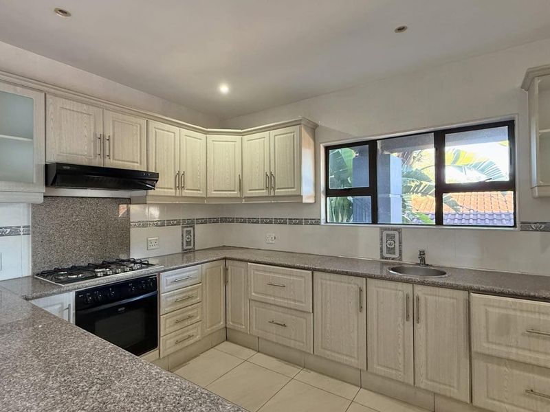 A clean, functional kitchen featuring light-toned cabinetry, granite countertops, a gas hob, built-in oven, and a tiled backsplash with a window view.