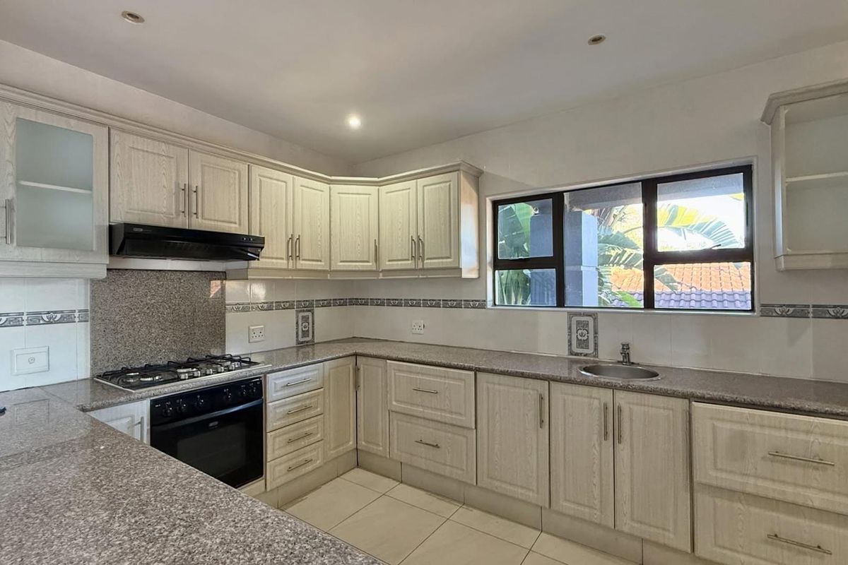 A clean, functional kitchen featuring light-toned cabinetry, granite countertops, a gas hob, built-in oven, and a tiled backsplash with a window view.