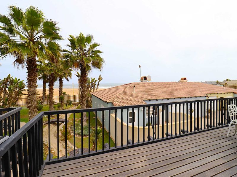 Elevated timber balcony overlooking a landscaped garden, palm trees, and the nearby coastline.
