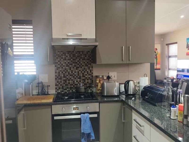 A functional kitchen featuring modern grey and white cabinetry, granite countertops, a gas hob with extractor fan, and a mosaic tile backsplash.