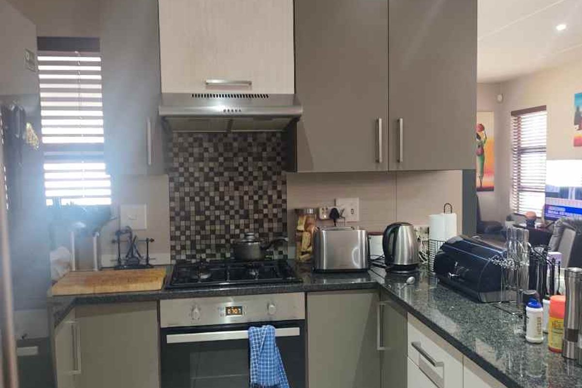A functional kitchen featuring modern grey and white cabinetry, granite countertops, a gas hob with extractor fan, and a mosaic tile backsplash.