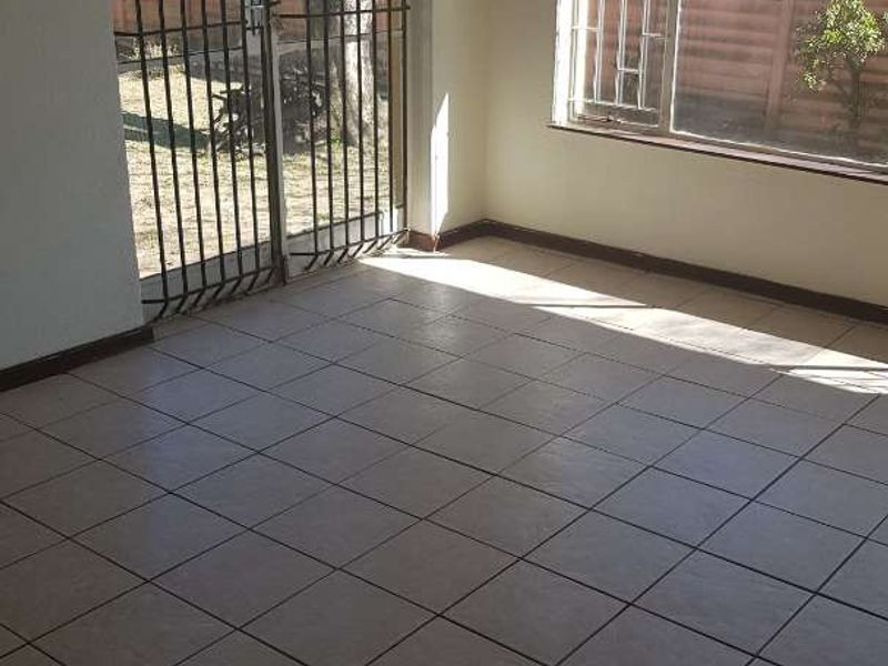 An empty living area featuring tiled flooring, large windows with burglar bars, and a security gate providing access to the exterior.