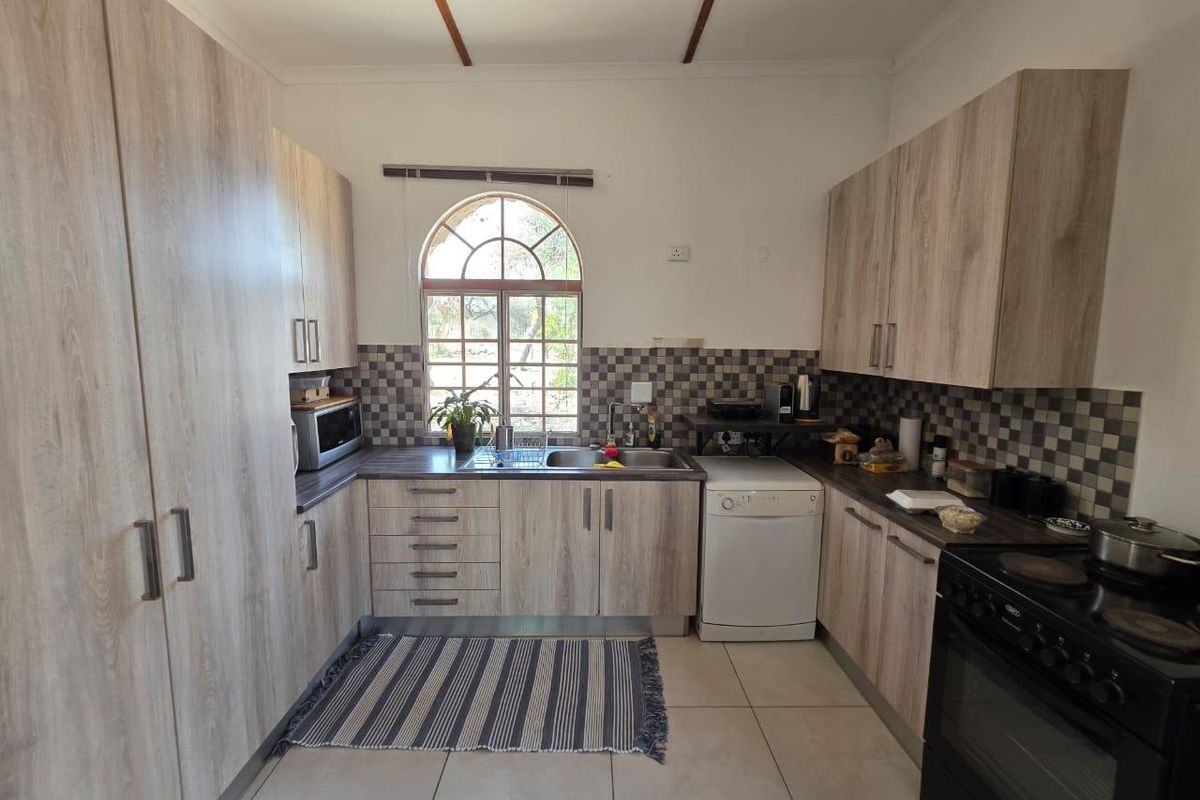 A functional kitchen featuring light wood-look cabinetry, a tiled backsplash, double sink, and an arched window providing natural light.