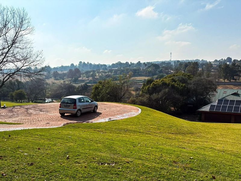 A scenic view of the property grounds featuring a circular brick driveway, expansive lawn, and a building equipped with roof-mounted solar panels.