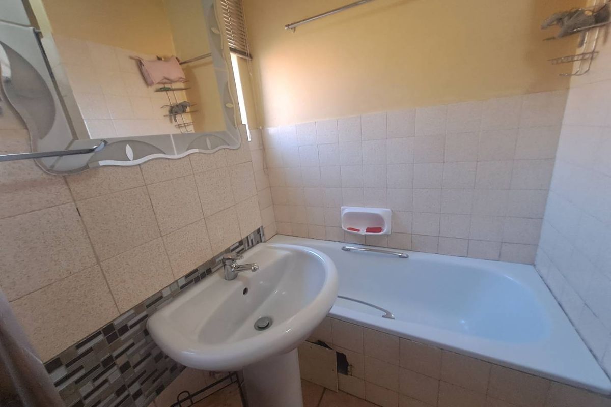 A functional bathroom featuring a pedestal washbasin and a standard bathtub with tiled splashbacks, requiring minor repairs and cosmetic updates.