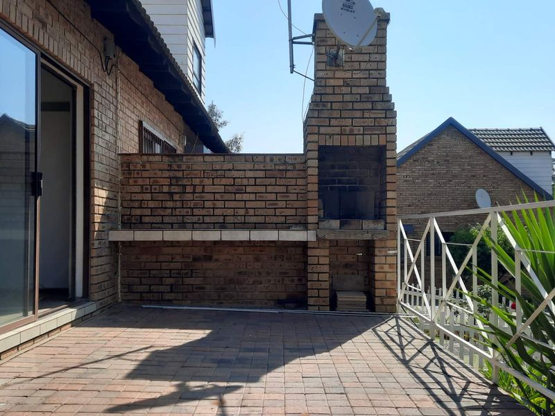 Outdoor patio area featuring a built-in brick braai, paved flooring, and a metal balustrade, providing a functional space for outdoor entertaining.