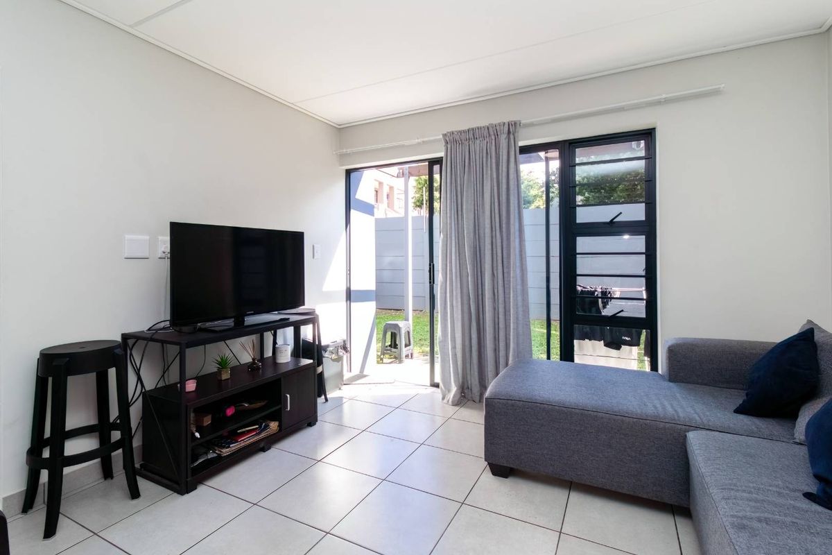 A bright living room featuring tiled flooring and large sliding glass doors that provide direct access to the outdoor patio and garden area.