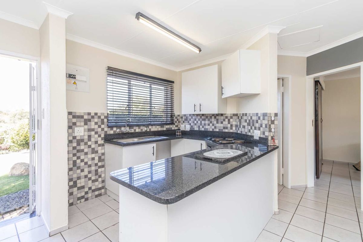 Compact kitchen featuring granite countertops, white cabinetry, a built-in hob, and a mosaic tile splashback, with direct access to the exterior.
