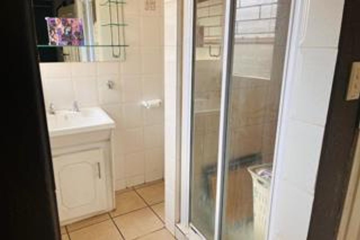 A functional bathroom featuring a vanity basin, shower enclosure, and tiled finishes throughout, offering potential for modernization.