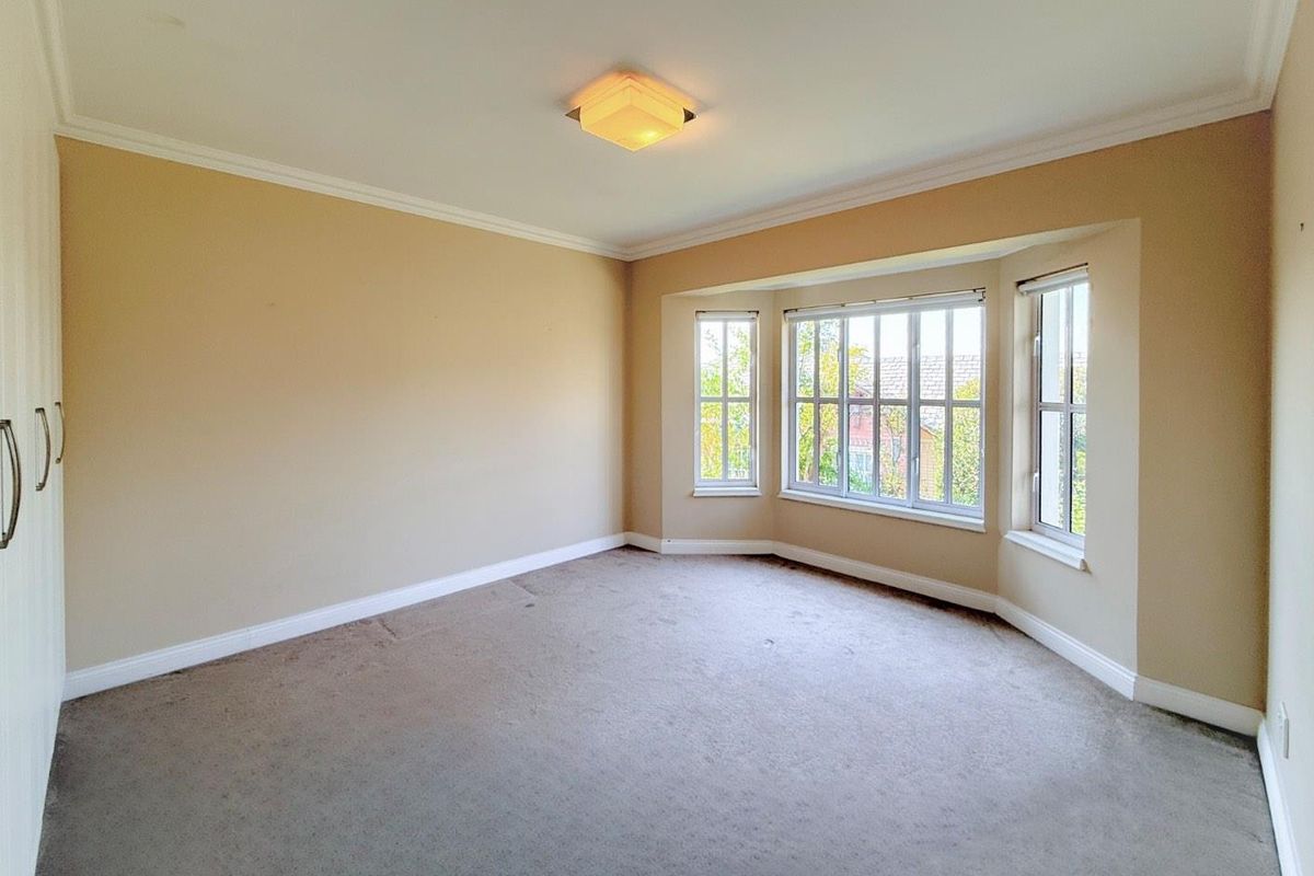 A spacious, empty bedroom featuring a large bay window, neutral wall tones, built-in wardrobe storage, and carpeted flooring.